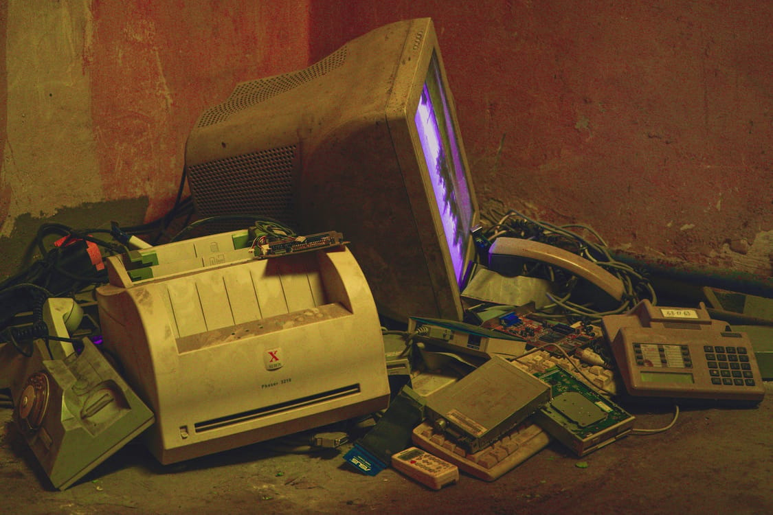 Several generations of laptops and smartphones on a workbench showing signs of repair, representing end-of-life electronics disposal obligations in Victoria